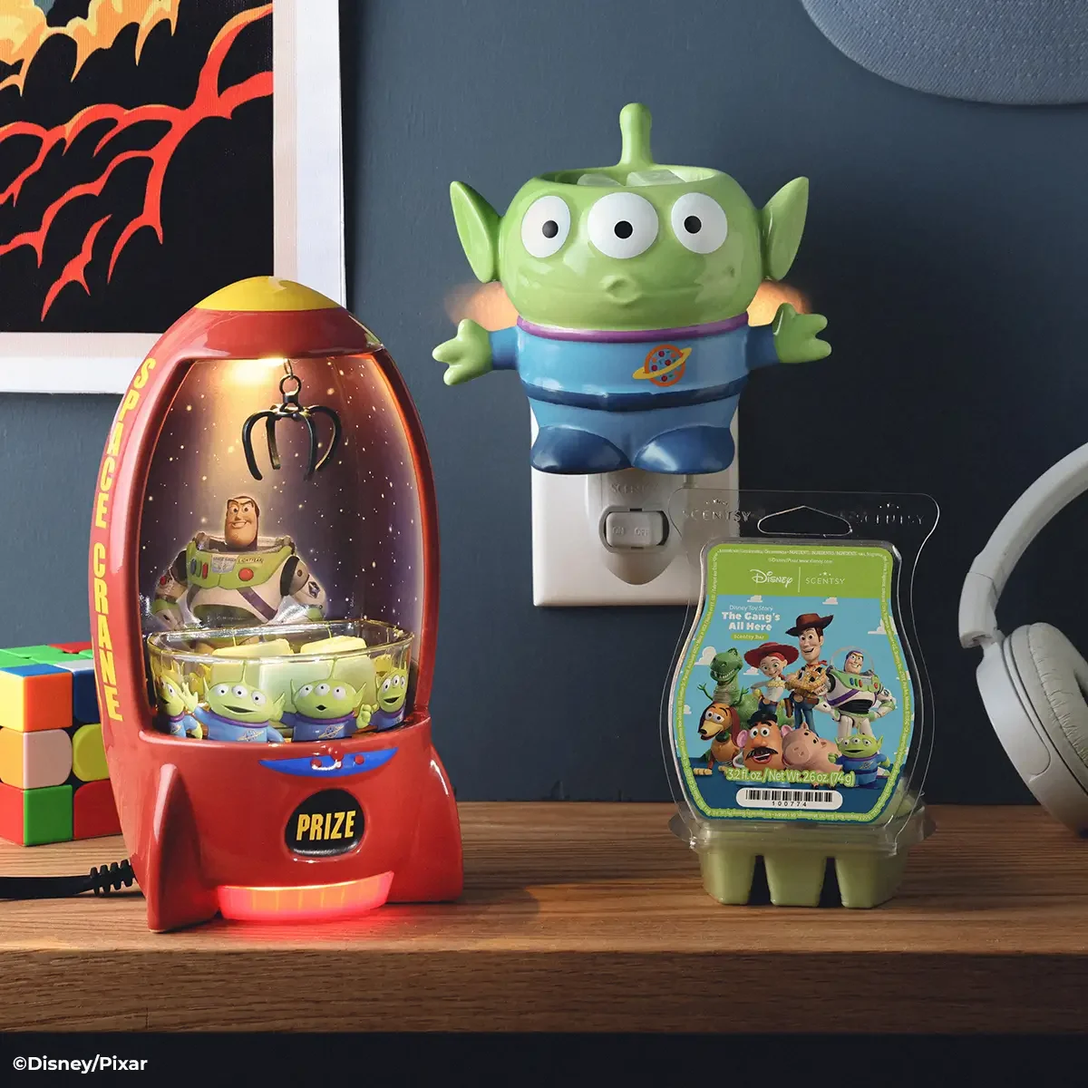 Toy Story Scentsy setup with Alien mini warmer plugged into wall, The Claw warmer glowing and Toy Story wax bar on desk