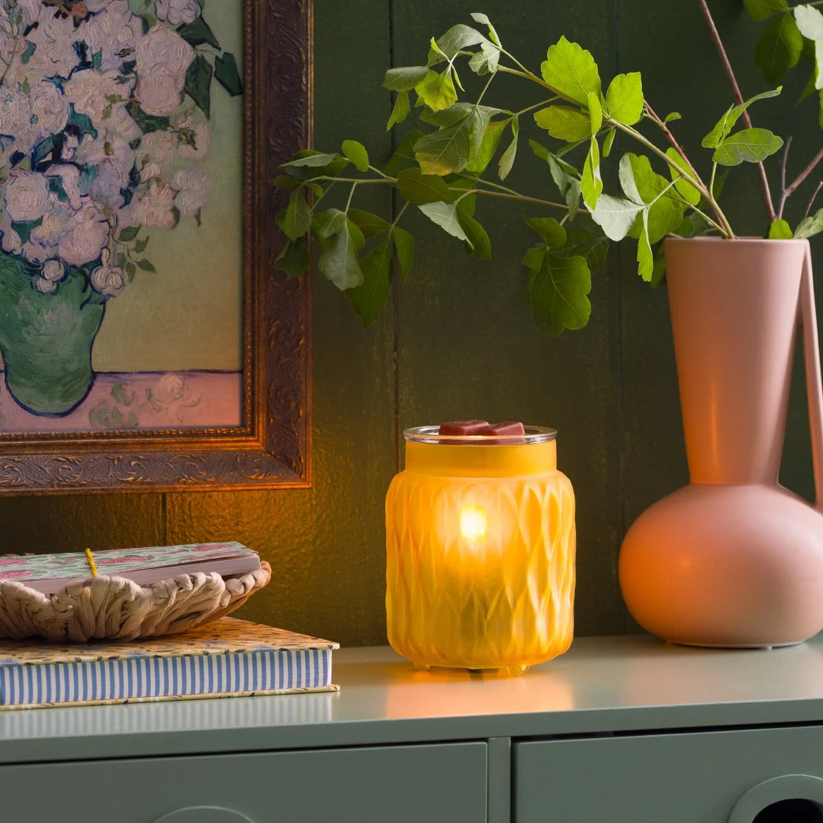 The Soft Honey Scentsy Warmer adds a warm golden glow to an enliven decor space, styled with soft green tones, modern vases, and layered textures for a cheerful, inviting look.