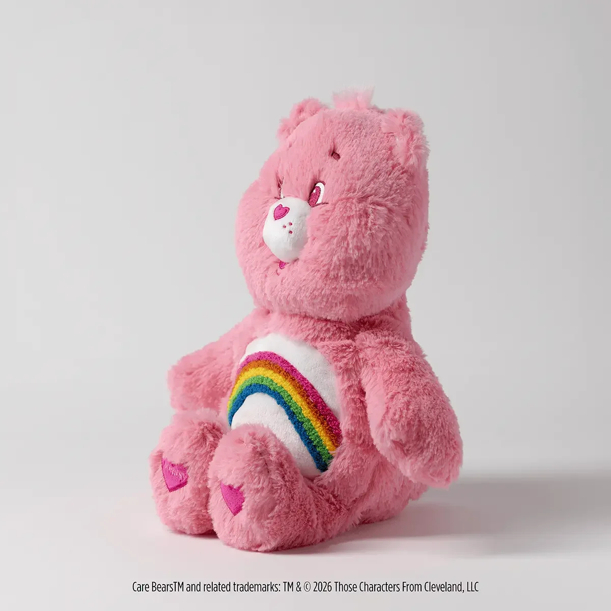 Cheer Bear Scentsy Buddy plush shown from the side with pink fur and rainbow belly badge