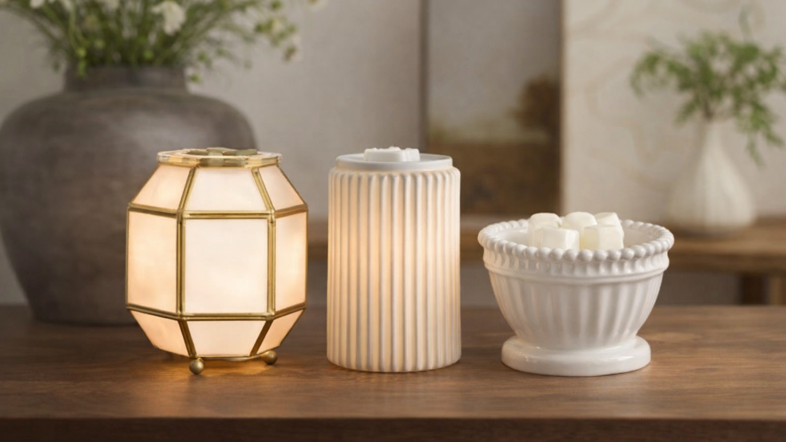 Three Scentsy Warmers displayed in a modern home setting, showcasing ceramic and glass warmer designs with warm light and neutral tones.
