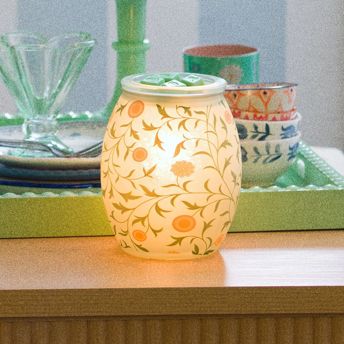 The Sunny Vines Scentsy Warmer features a cylindrical design with hand-painted vine and floral motifs. When illuminated, the warmer casts a soft glow that enhances its airy, botanical pattern.