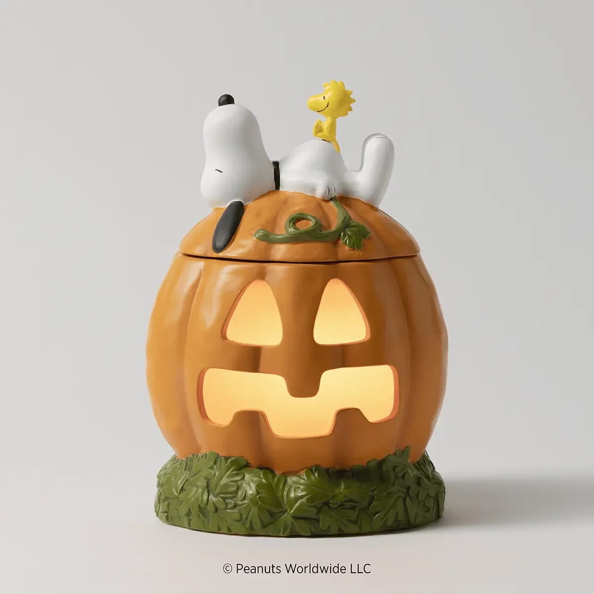 Snoopy's Pumpkin Patch Scentsy Warmer illuminated with a warm golden glow shining through the jack-o'-lantern face, with Snoopy and Woodstock resting on top.