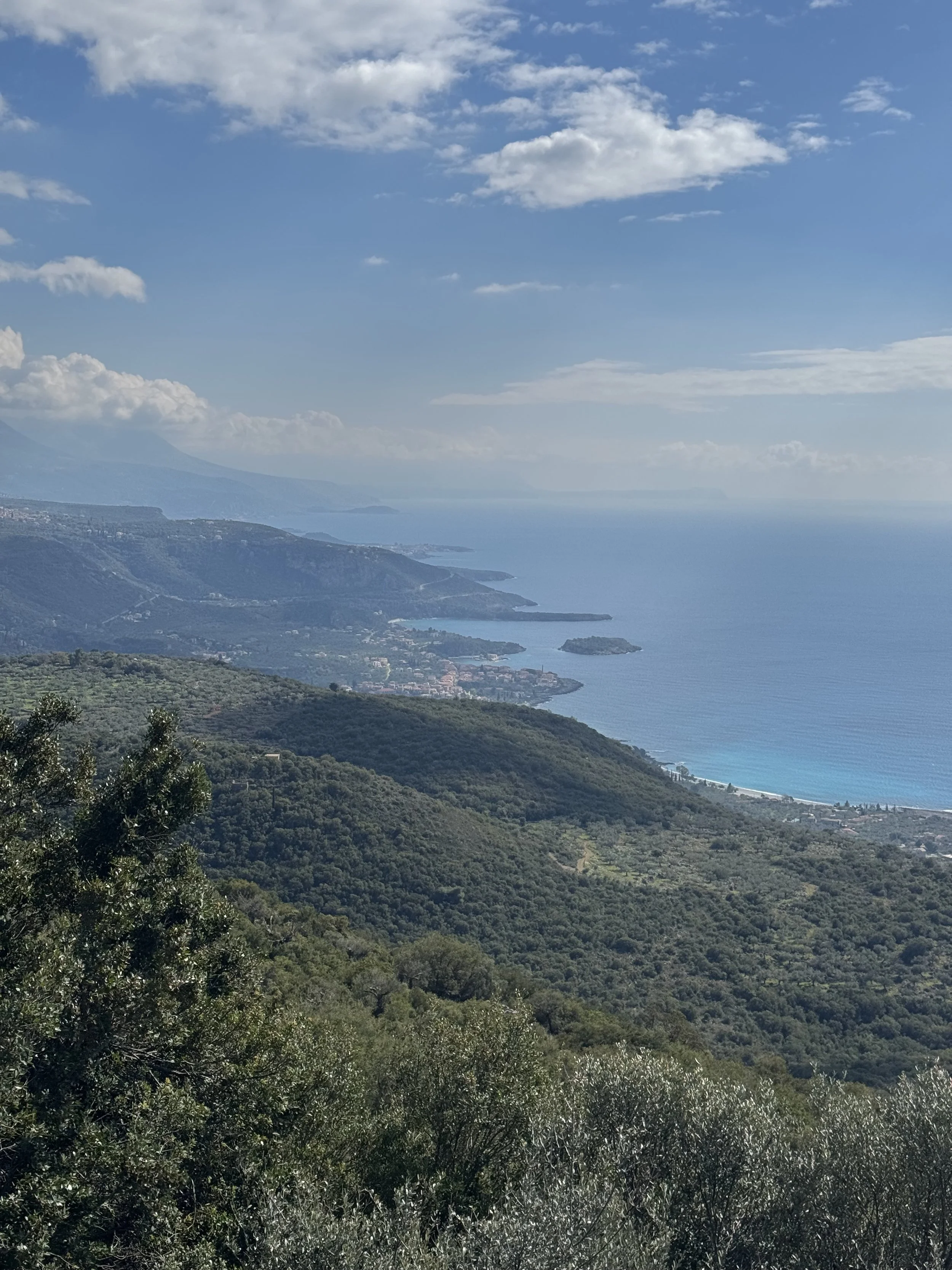 Scenic view of mountains, coastline, and ocean under a blue sky with scattered clouds.