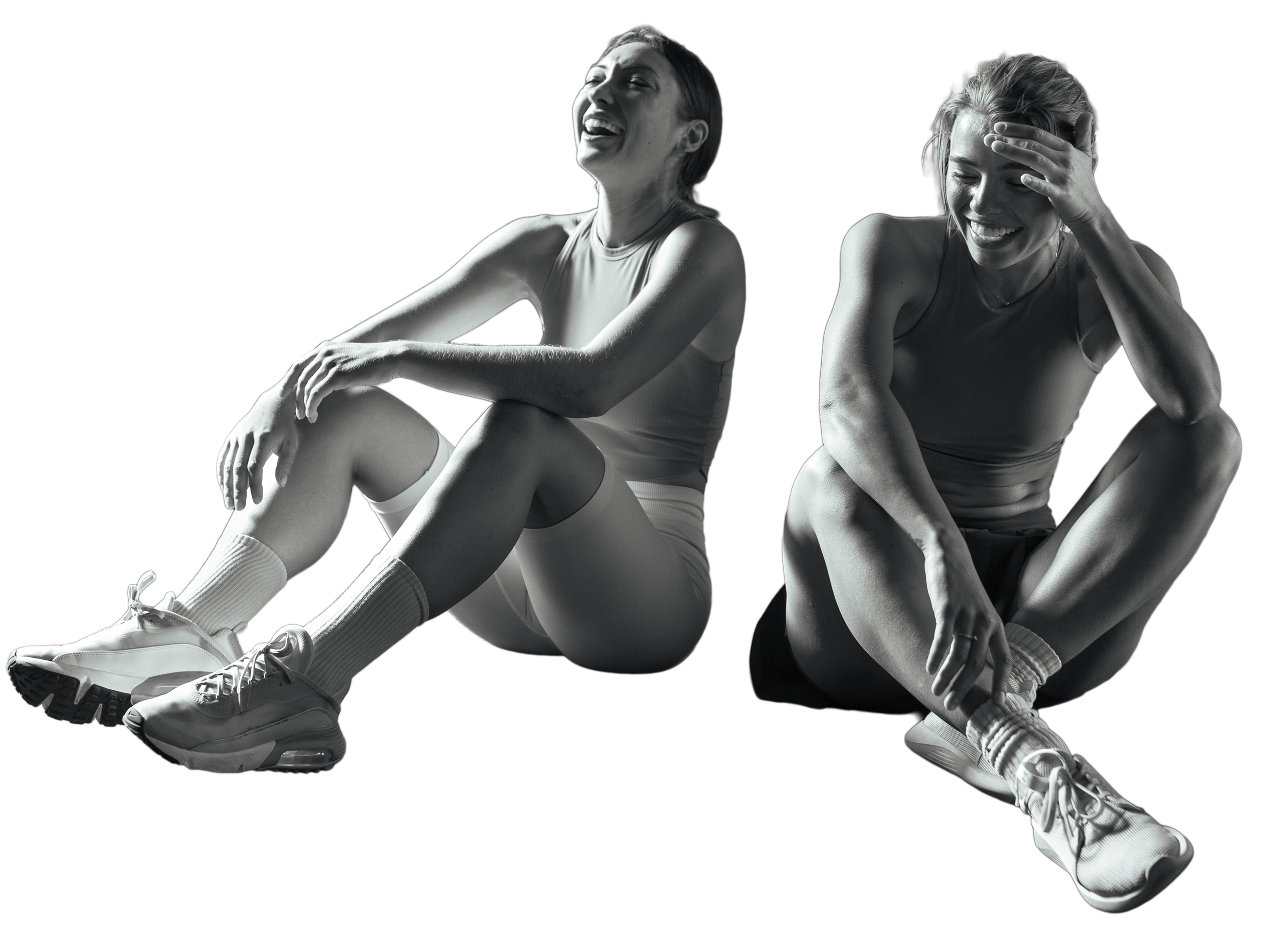 Two women sitting on the ground, wearing workout clothes and sneakers, laughing and enjoying each other's company.