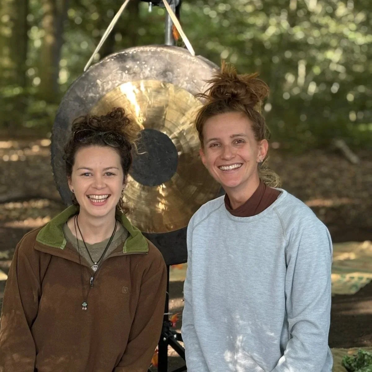 Two women smiling in front of a gong set in a woodland