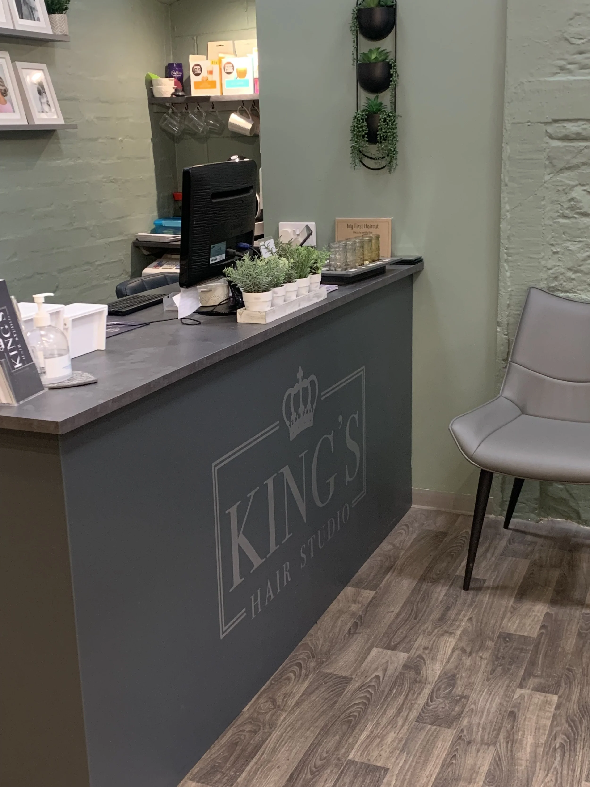 Reception area of King’s Hair Studio with a counter, computer, small plants, and a modern chair.