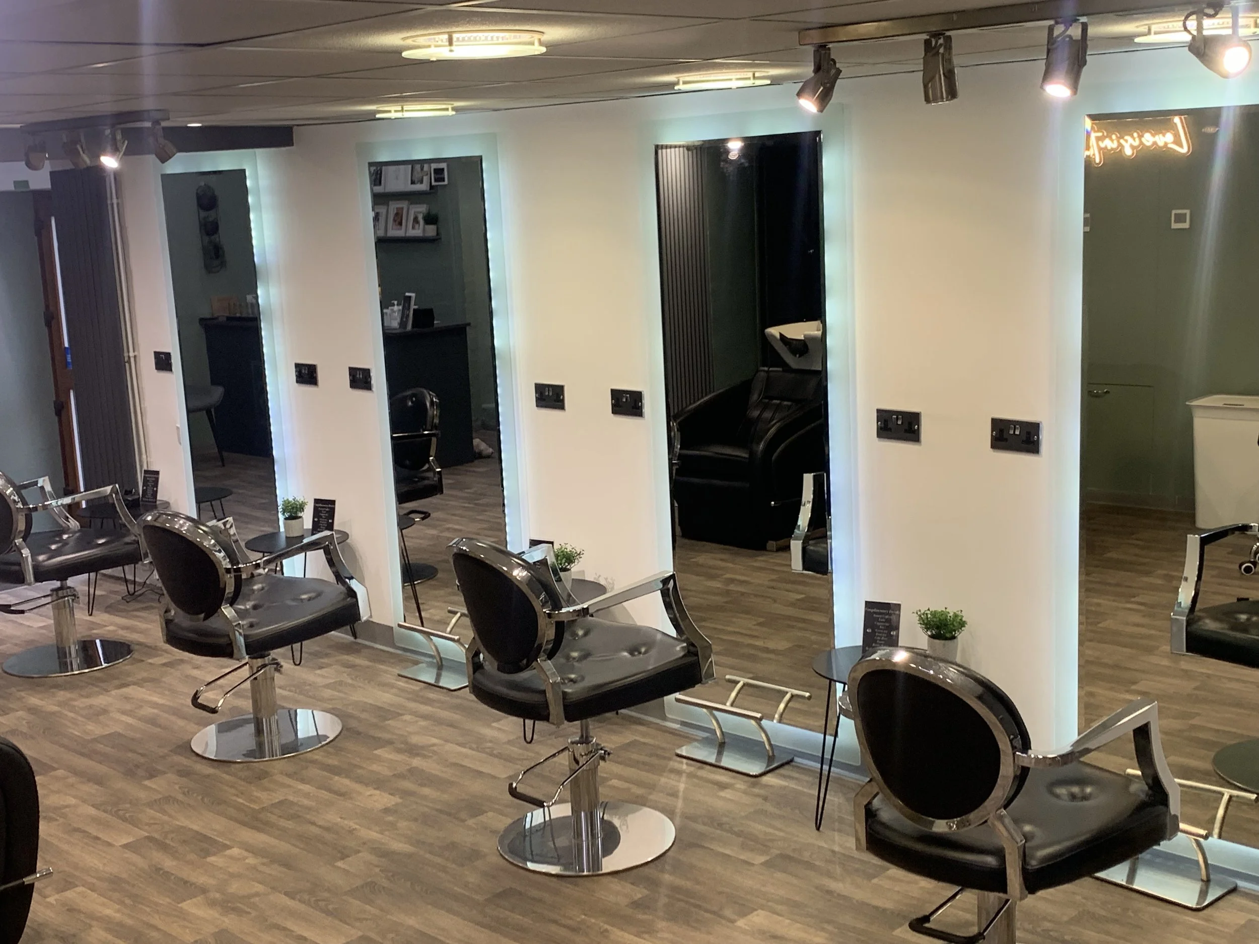 Hair salon with black salon chairs, small tables, and mirrors, illuminated by overhead lighting, with a massage chair in one of the cubicles.