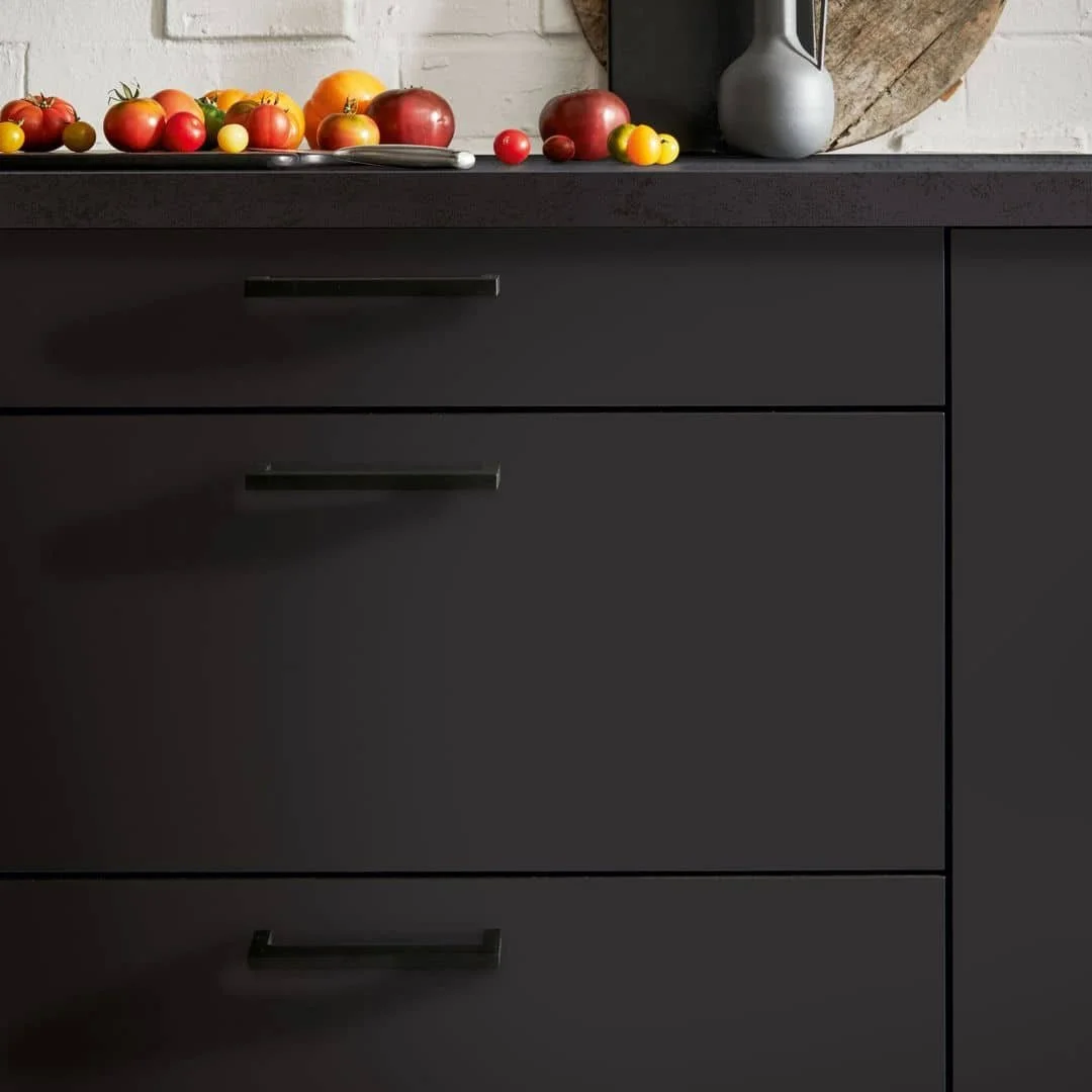 Black kitchen cabinet with several tomatoes and yellow cherry tomatoes on a tray or plate on the countertop, and a gray vase nearby.