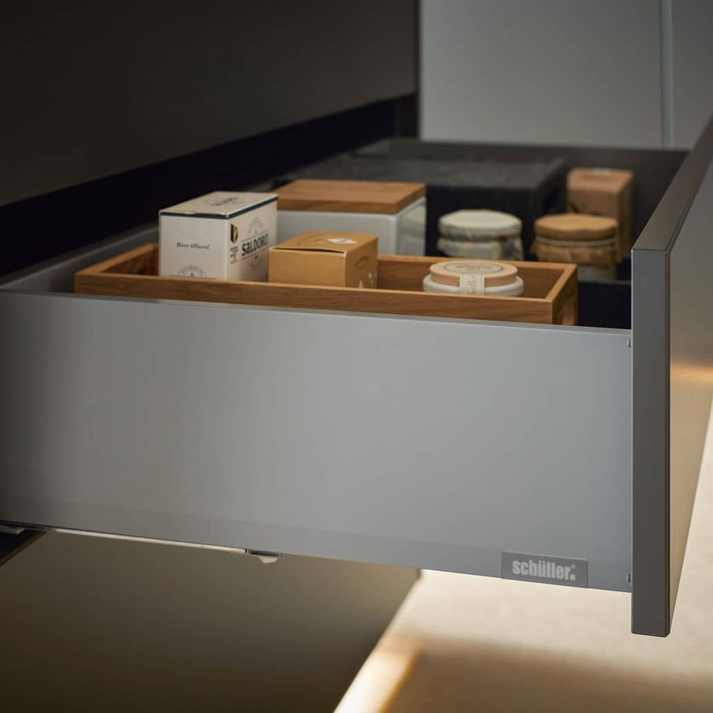 Open drawer containing various packaged food items on wooden and black trays.
