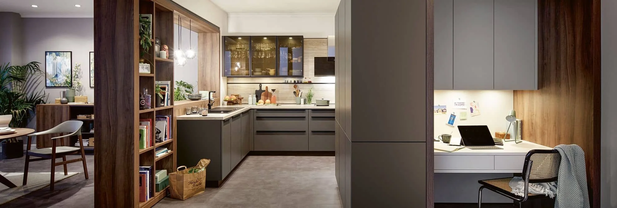 Modern kitchen with dark gray cabinets, wooden accents, and a small home office area with a desk and chair.