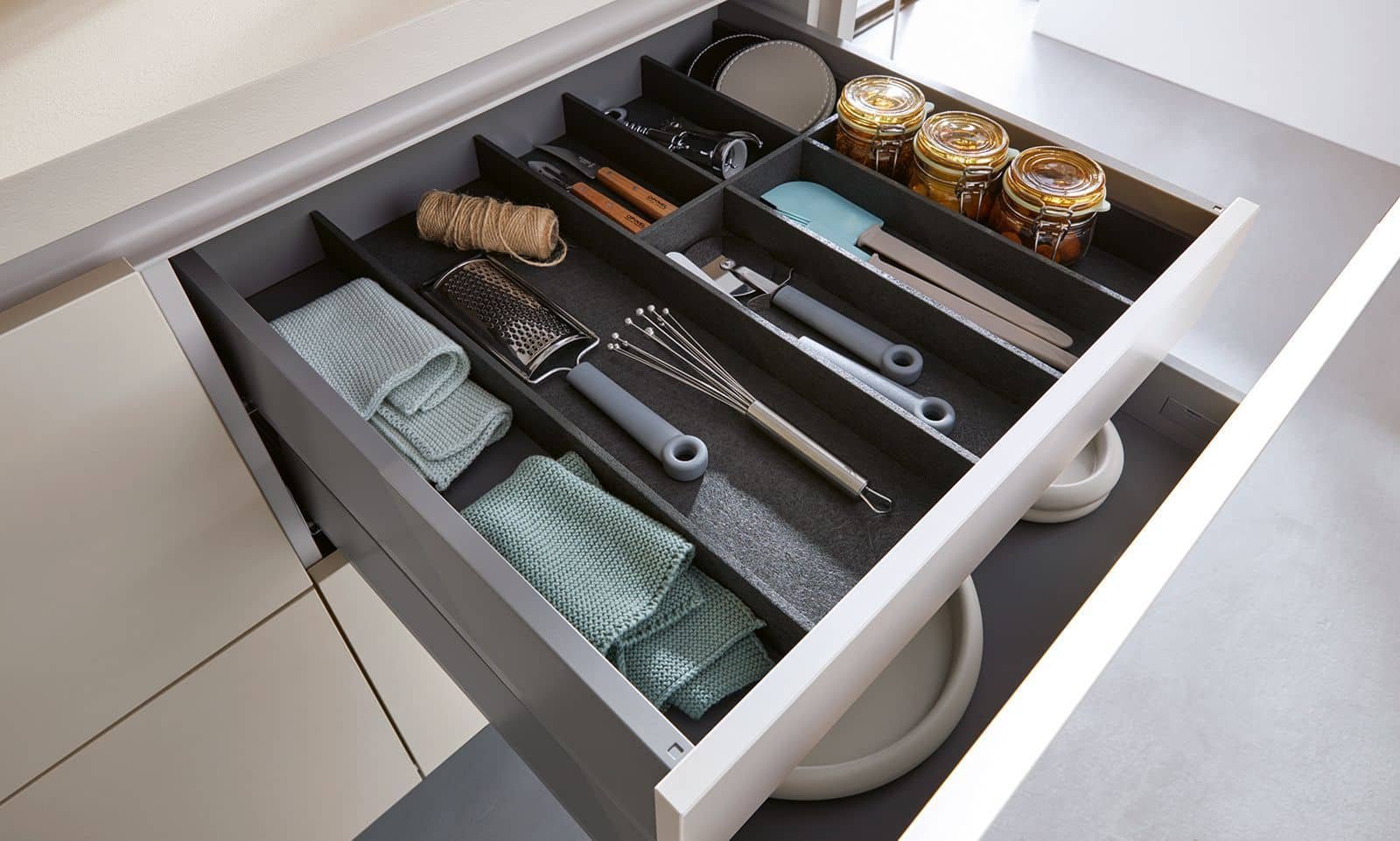Open kitchen drawer containing kitchen utensils, towels, and jars of preserves.