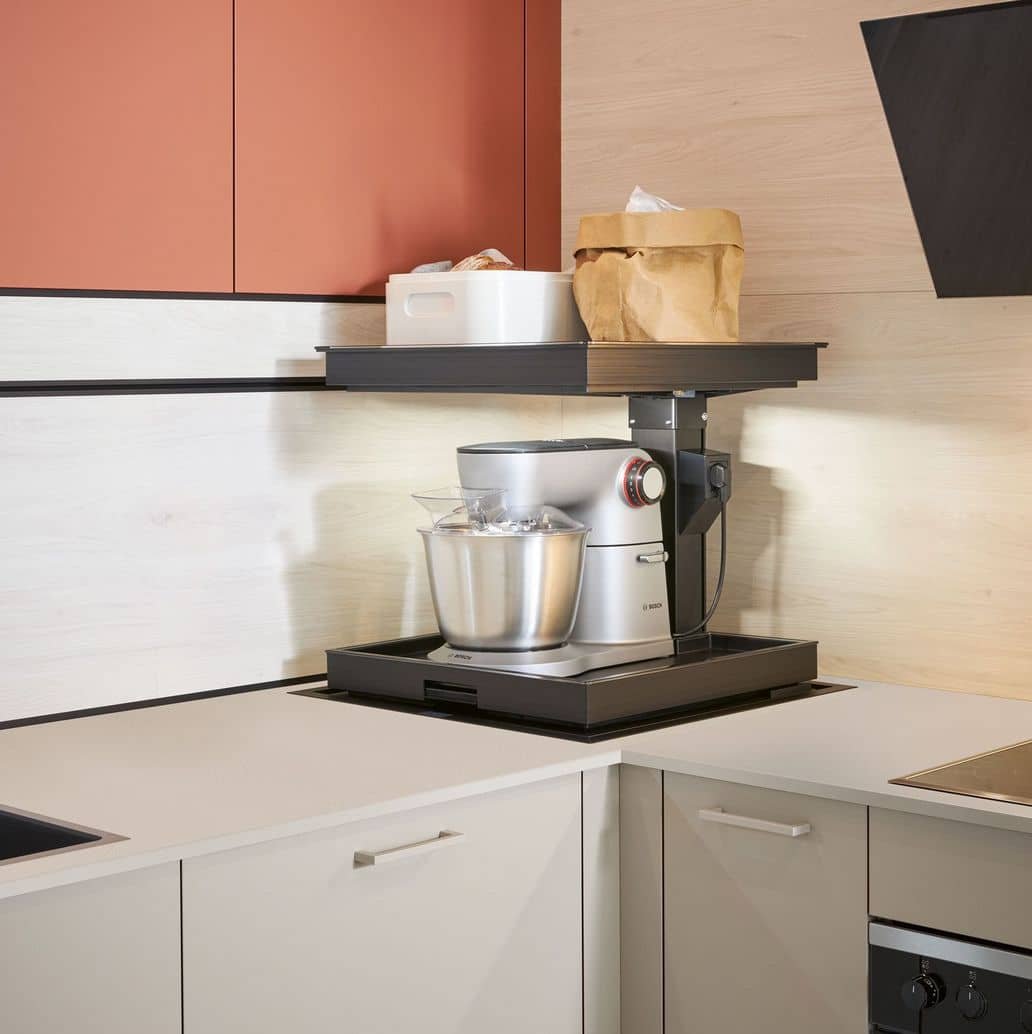 Kitchen counter with a stand mixer, metal bowls, a white box, and a brown paper bag on a black shelf above.