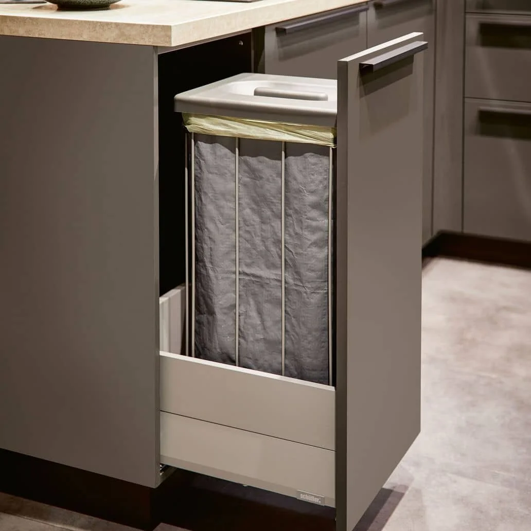 A kitchen cabinet door is open, revealing a trash can with a fabric liner inside a pull-out cabinet.