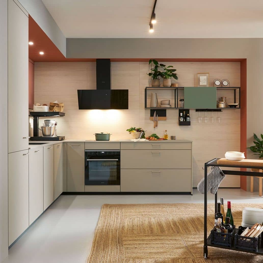 Modern kitchen with light grey lower cabinets, black countertop, open shelving, potted plants, and kitchen appliances on light wood panel wall with beige and terracotta accents.