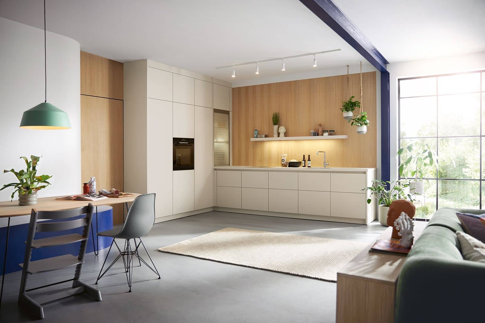 Modern kitchen and living room with large window, white cabinetry, wooden accents, green plants, and minimalist decor.
