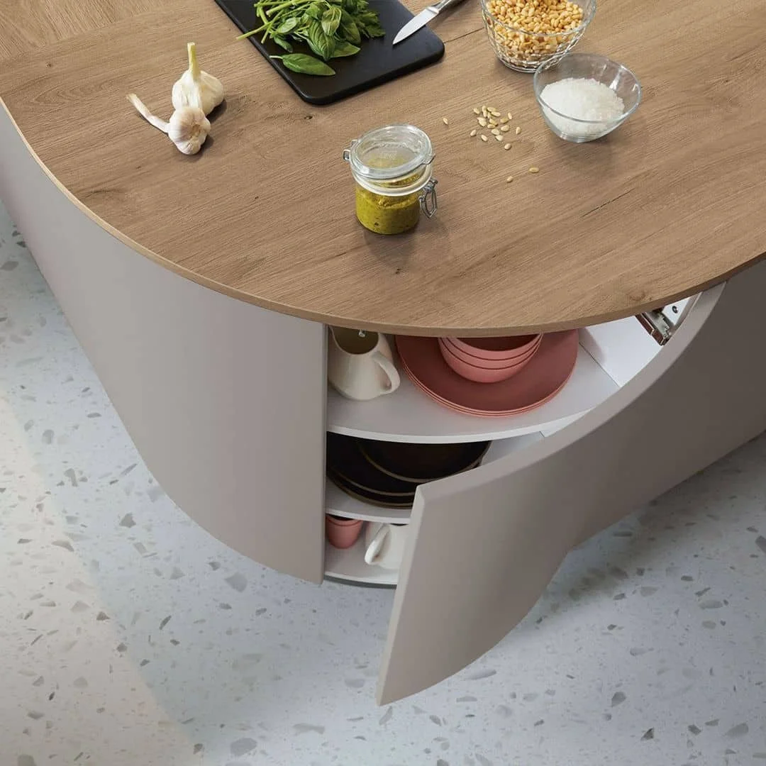 Kitchen island with garlic, fresh herbs, and cooking ingredients on top; open cabinet with pink plates and black bowls inside.