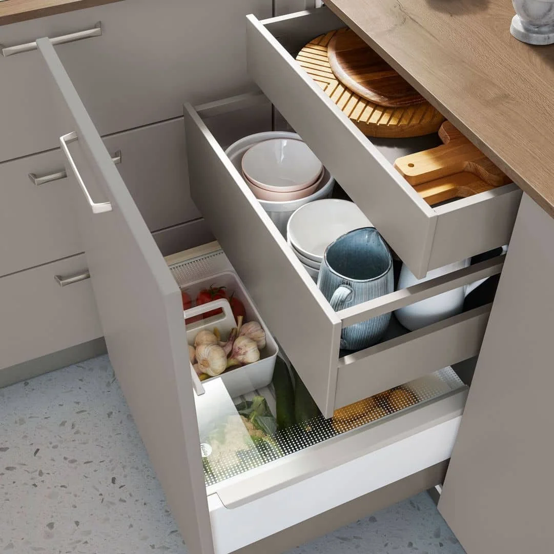 Open kitchen drawers filled with bowls, cutting boards, garlic, cherry tomatoes, and vegetables.