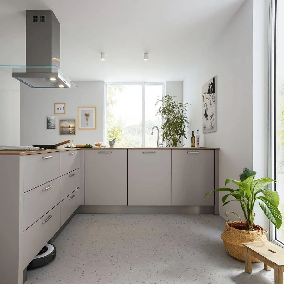 Modern kitchen with white cabinets, large window, potted plant, and minimalist decor.