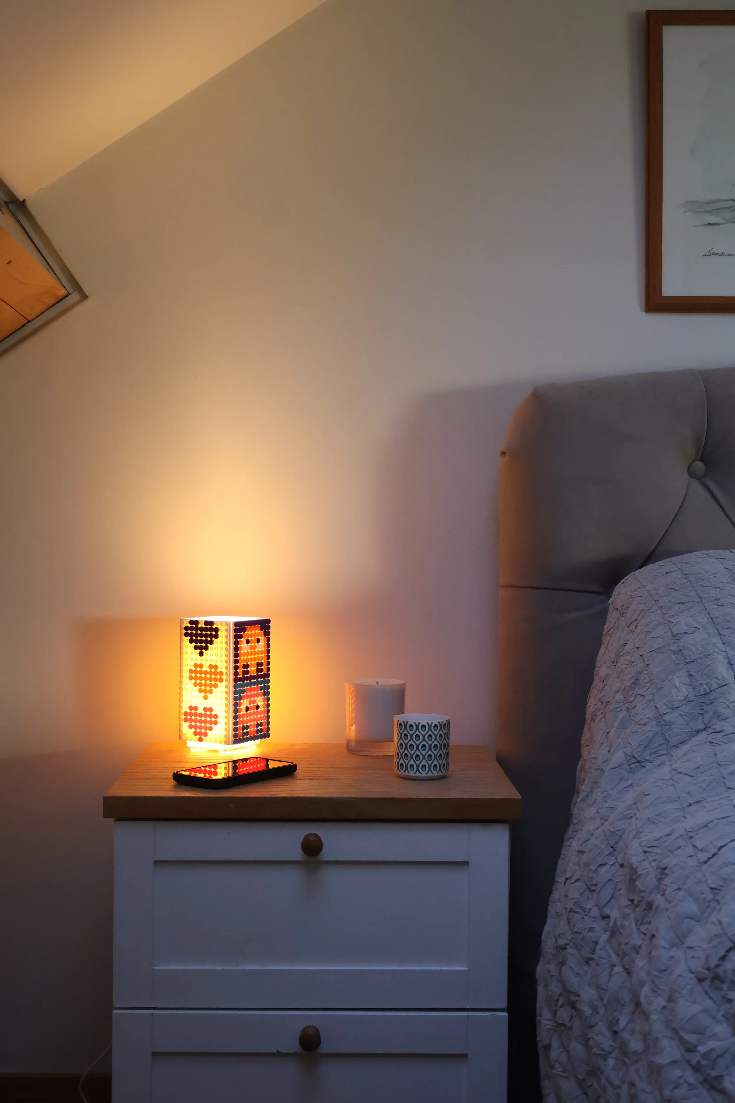 A Jaim mood lamp nightlight on a bedside table. Featuring a cute red heart design on one side and retro Pac-Man style alien pixel art on the other.