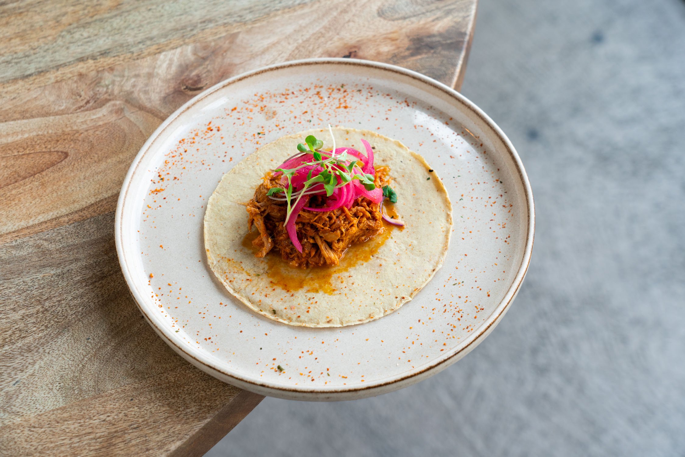 Taco con carne deshebrada, cebolla encurtida, microgreens y especias en plato blanco