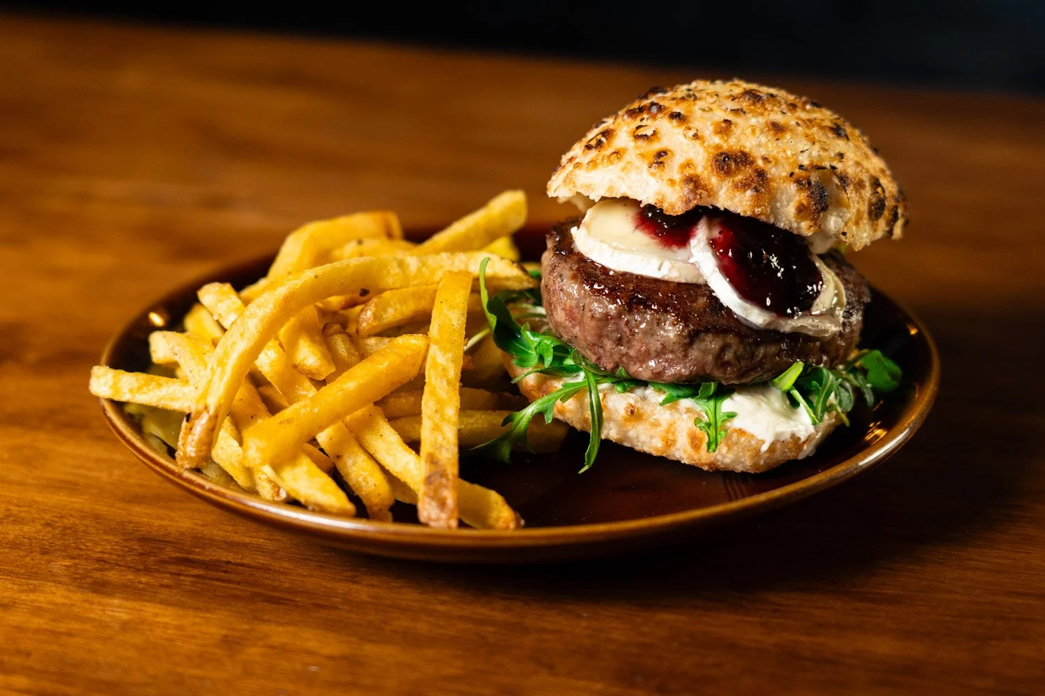Hamburguesa con patatas fritas en un plato de cerámica, con carne, queso, salsa y pan, en una mesa de madera.