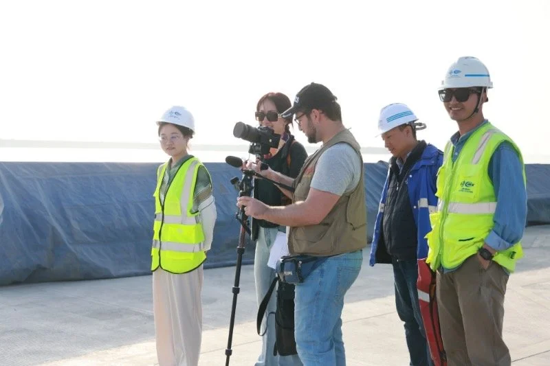 David Amar Foto con equipo de videografía trabajando junto a grupo de ingenieros y personal en un sitio de construcción o infraestructura, algunos con cascos y chalecos de seguridad.