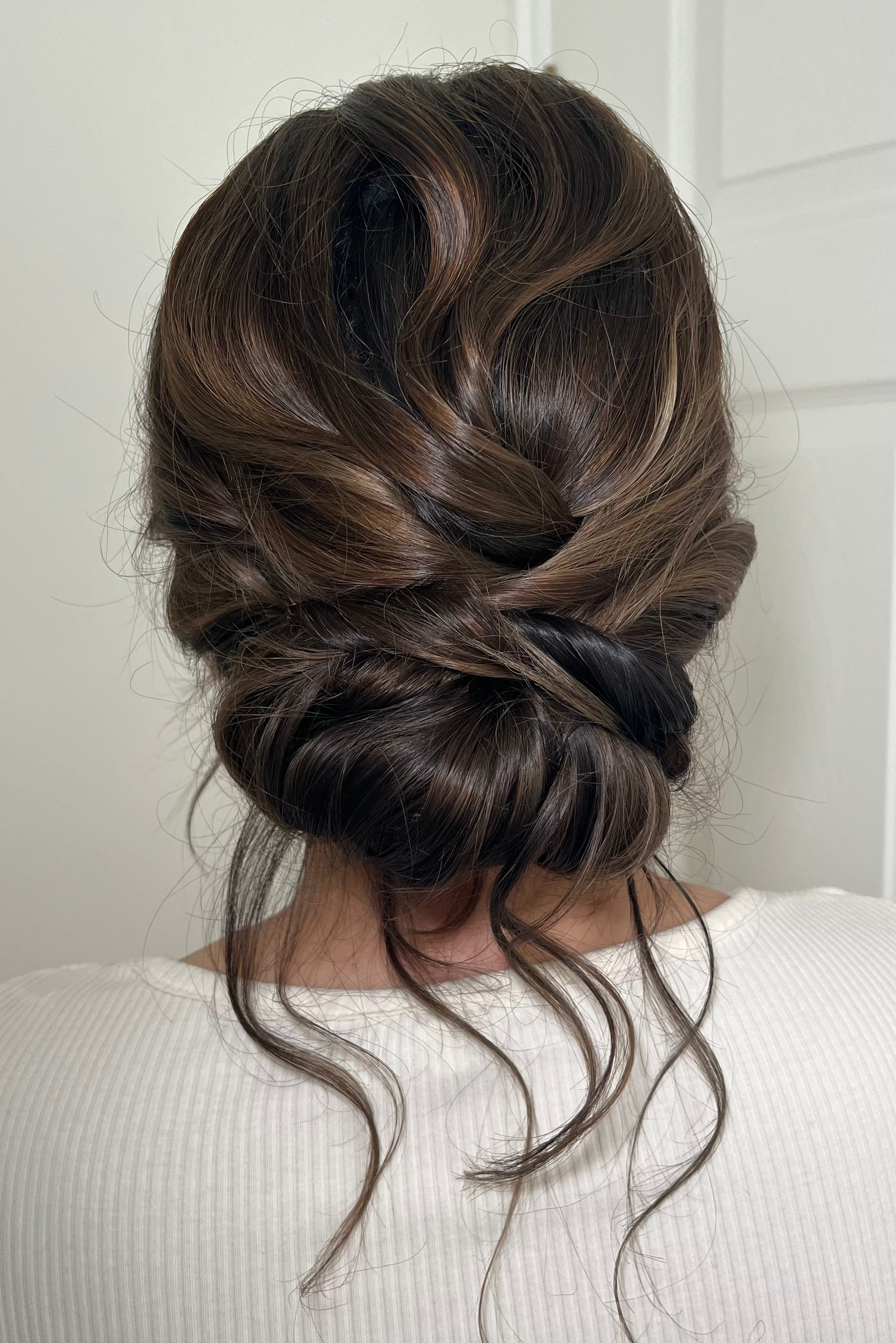A bridal hair style up in a textured low bun, styled on dark hair.