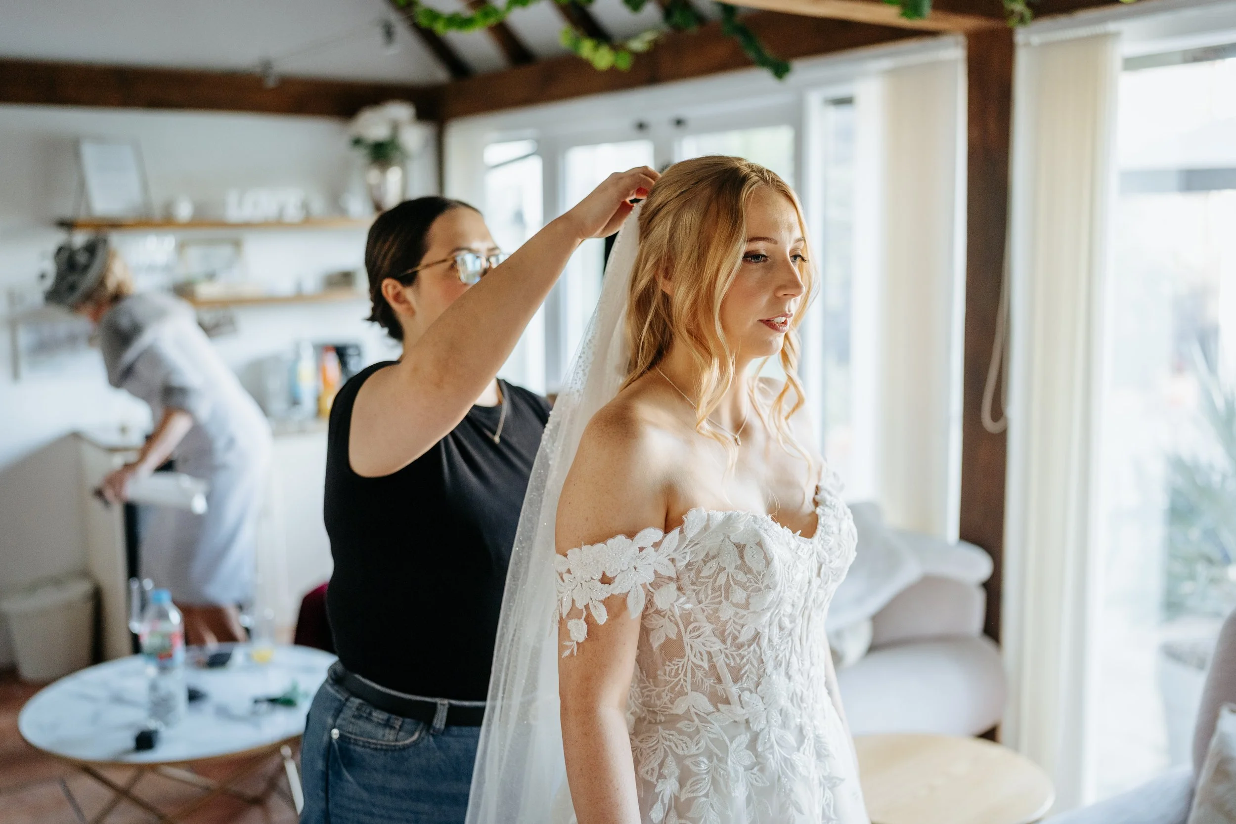 A bride having her veil fitted on her wedding morning, wearing modern, natural hair and makeup ready for her wedding at High House in Essex.