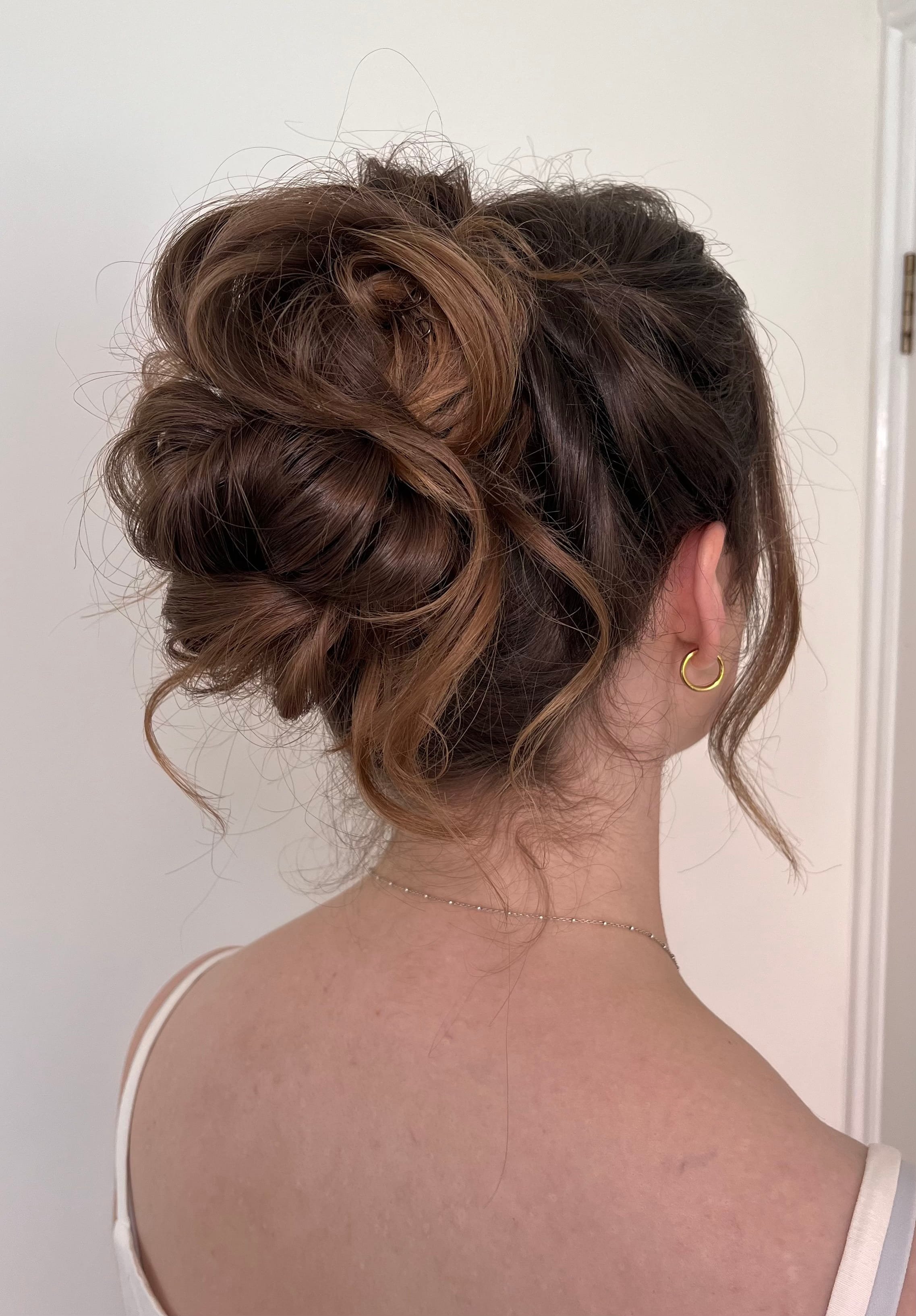 A messy, high bun bridal updo hairstyle created on long, dark hair.