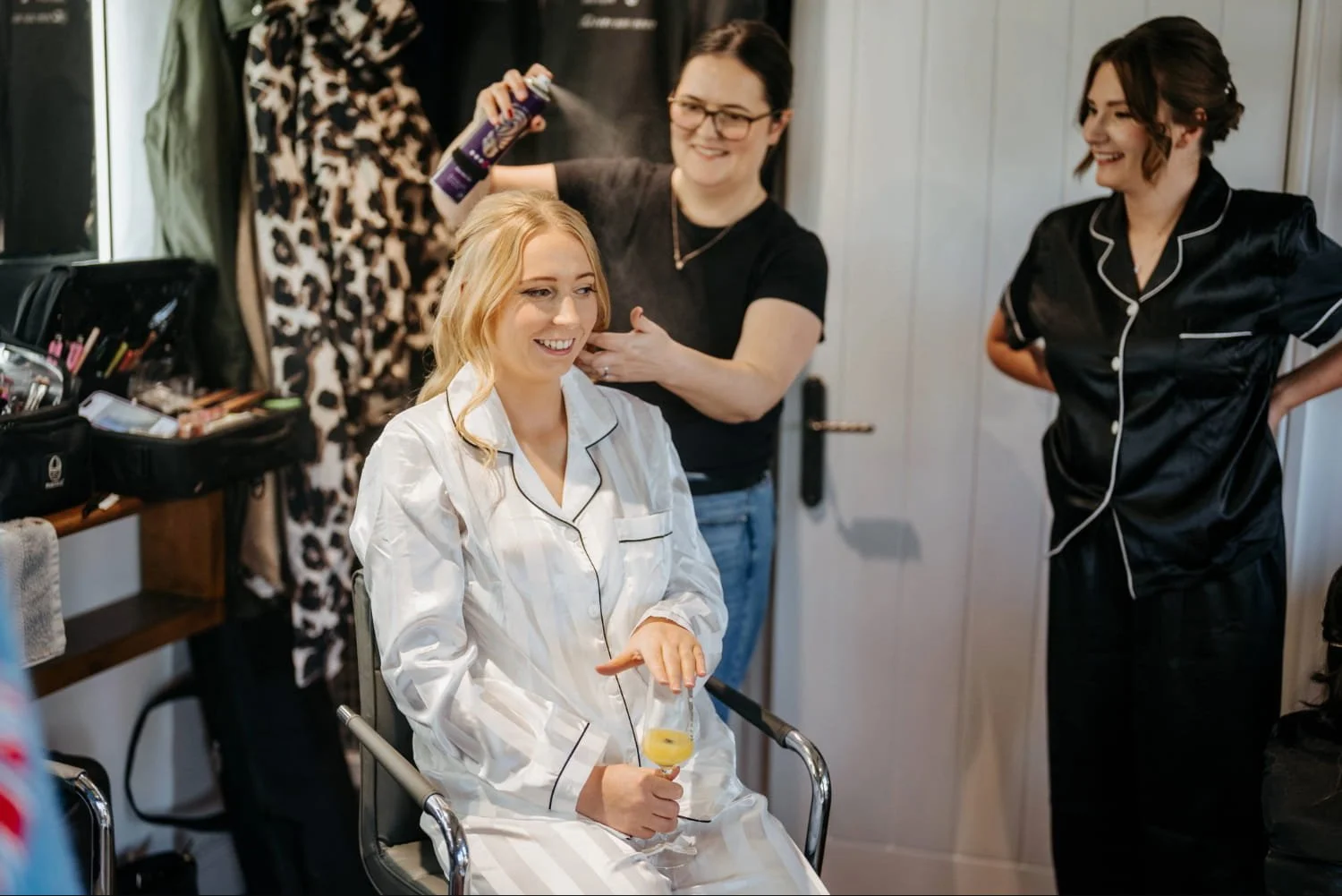 A bride with her wedding hairstylist and bridesmaid, having final touches made to her bridal hairstyle before her wedding at High House in Essex.