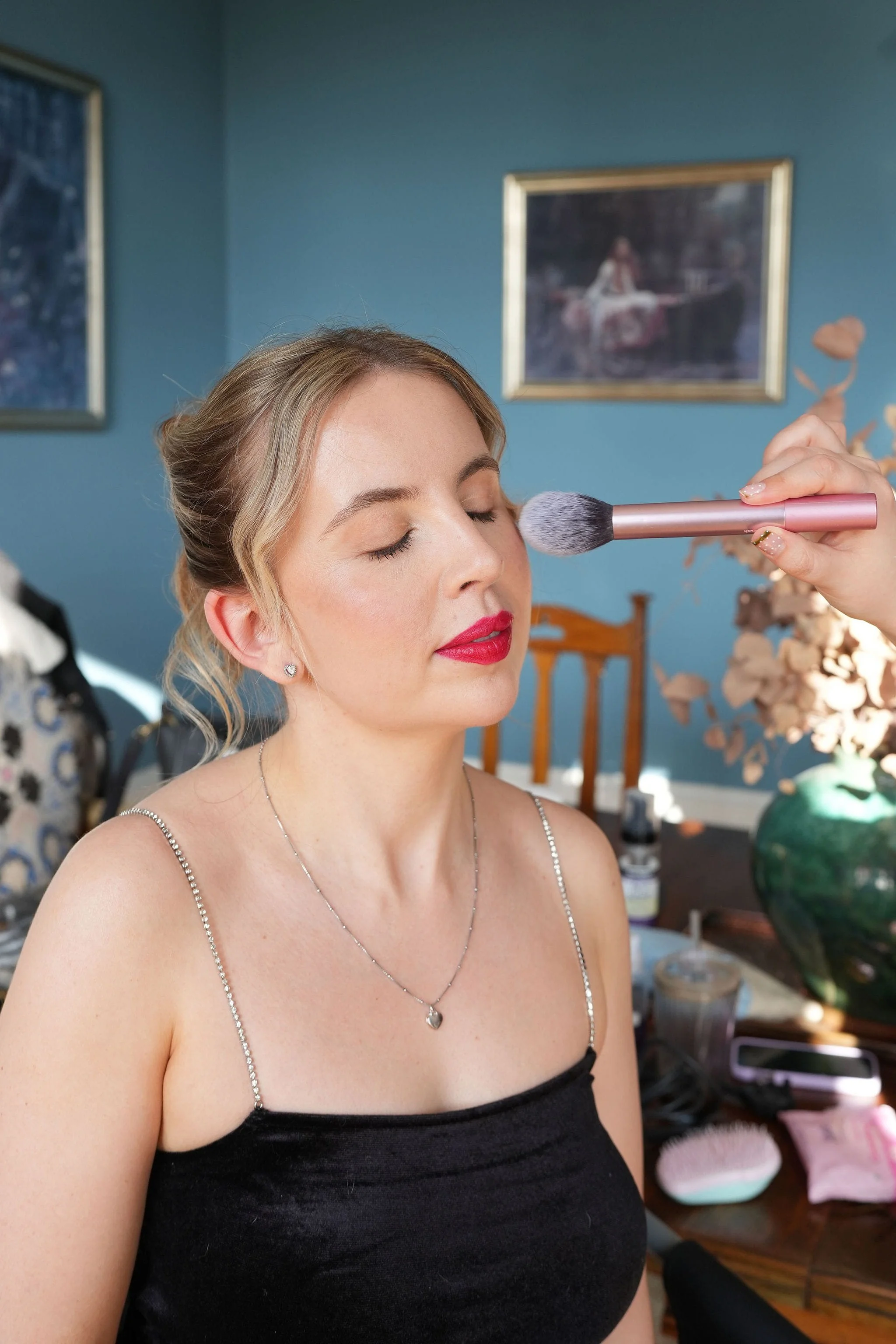 A woman having her makeup applied with natural skin and a red lip ready for an event at Alresford Hall in Essex.
