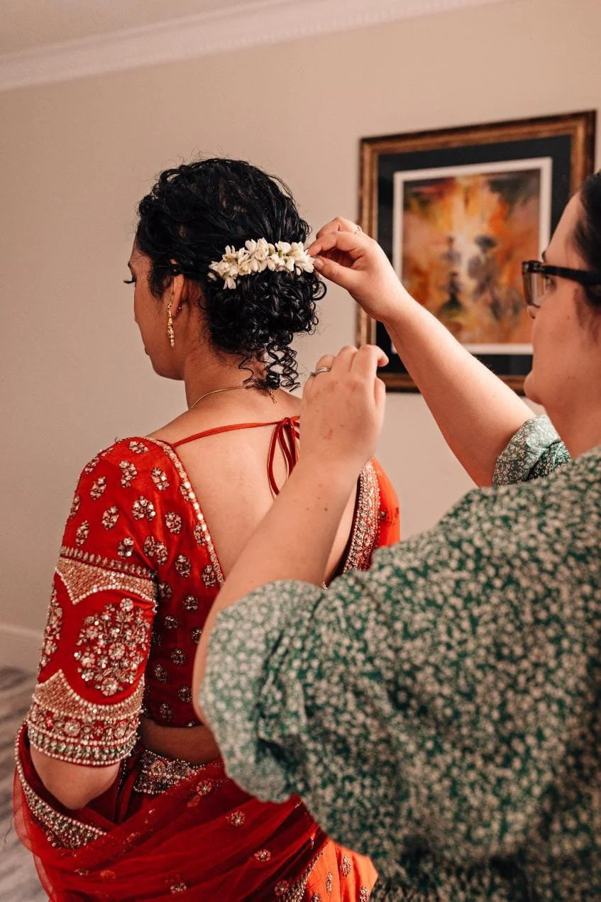 A bride wearing a lehenga, having accessories placed in her wedding hairstyle using her natural curls at Greyfriars Hotel Colchester.
