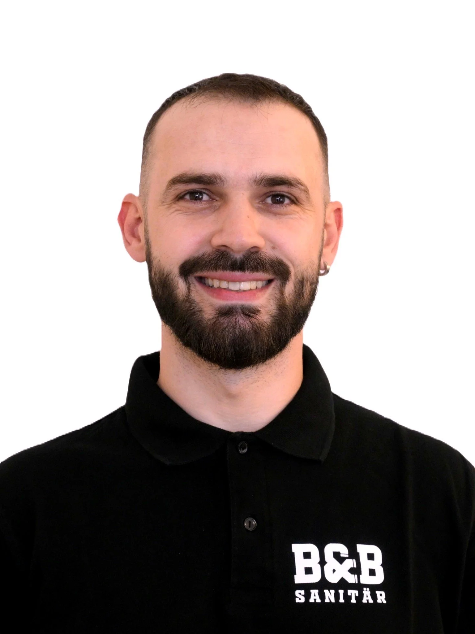 Mann mit dunklem Haar, Bart und Earring trägt schwarzes Polo mit Logo 'B&B SANITÄR' auf weißem Hintergrund.