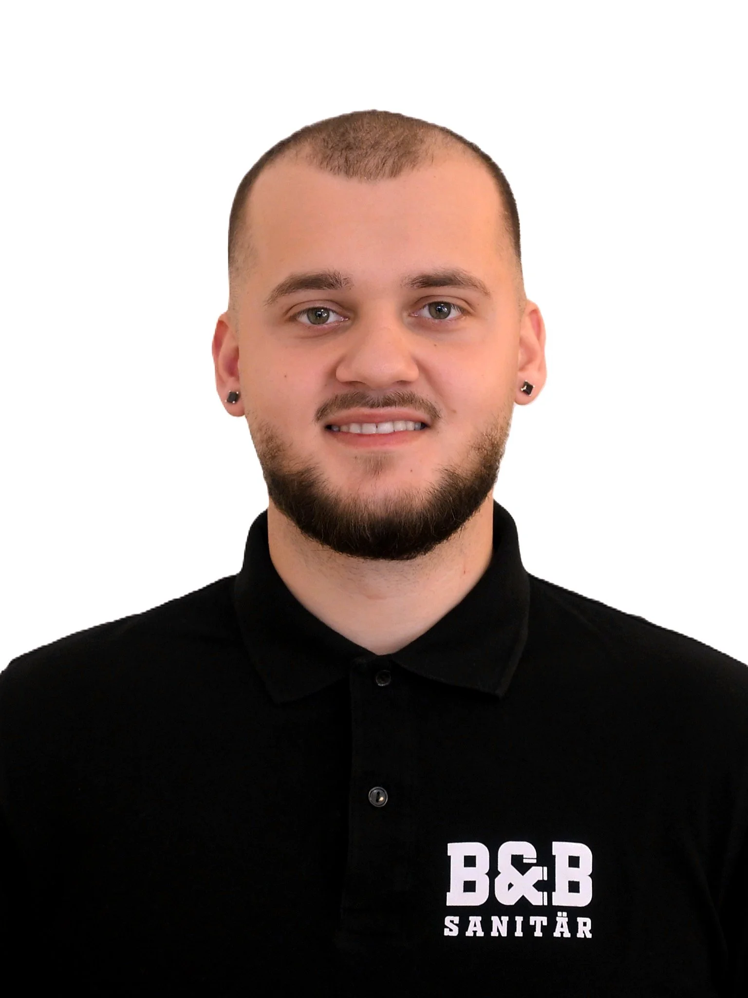 Ein Mann mit kurzen Haaren, Bart, schwarzen Ohrringen und einem schwarzen Polo-Shirt mit dem Logo 'B&B Sanitär'.
