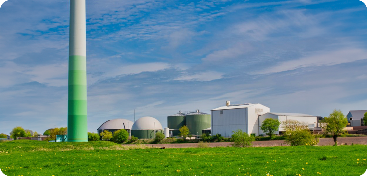 Industrial facility with wind turbine, storage tanks, and green landscape under blue sky.