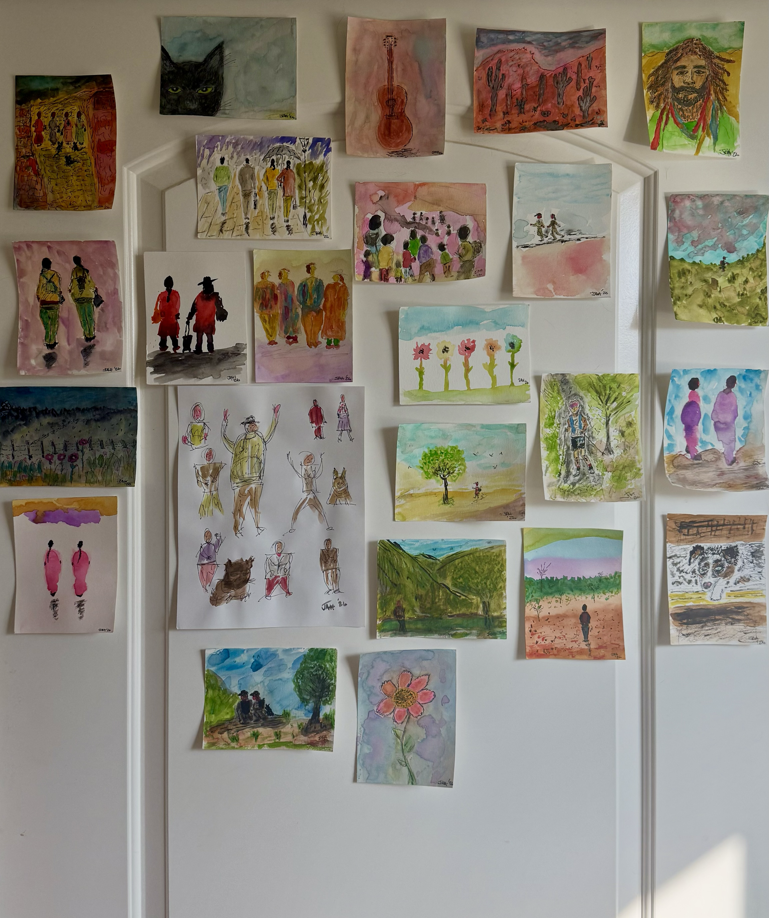 A display of watercolor paintings on a wall, featuring various scenes and subjects including people, landscape, animals, and abstract designs.