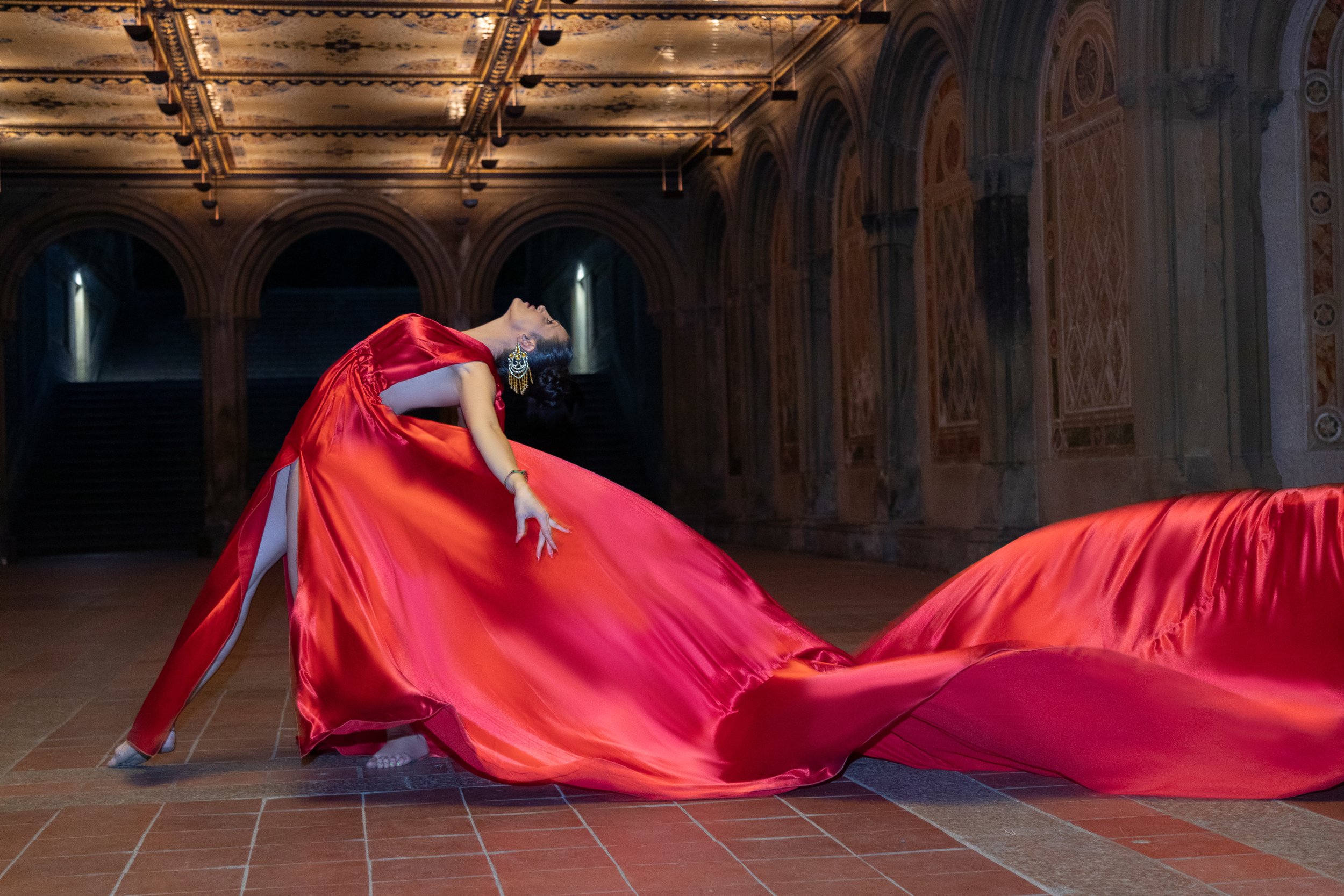 Dancer in a flowing red dress posing dramatically in an ornate hallway.