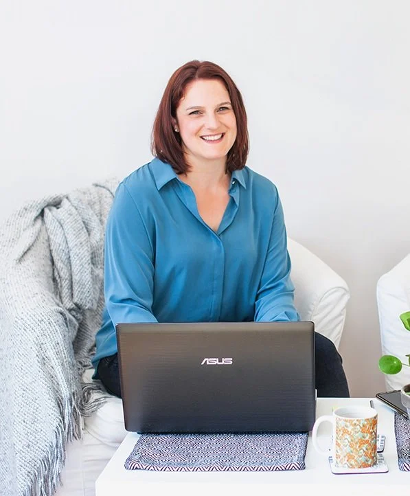 Erin an EMDR Therapist Houston wearing blue blouse smiles while sitting in white chair behind laptop