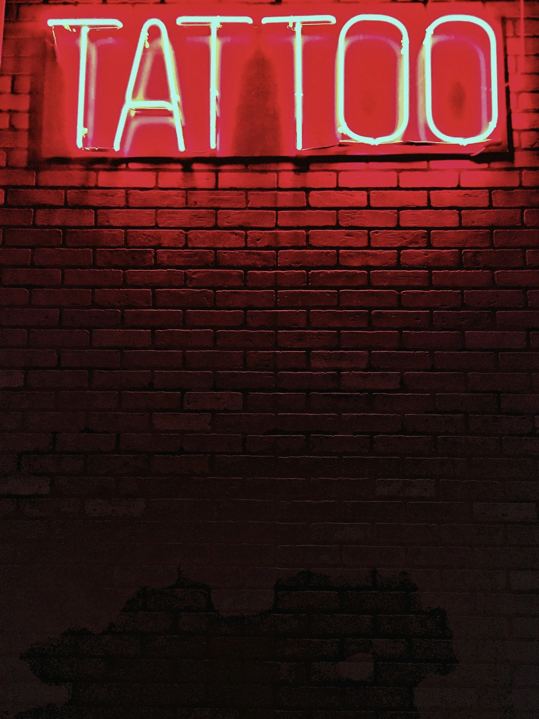 Red neon sign with the word "TATTOO" mounted on a brick wall.