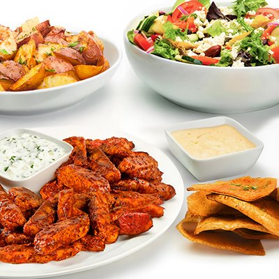 A photo of the spicy harissa chicken family feast, showing strips of grilled chicken covered in harissa sauce, a side of roasted potatoes, and a bowl of greek salad