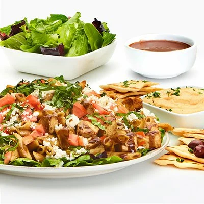 a photo of the signature pasta family feast, with a large plate loaded with penne pasta, cubed grilled chicken fresh herbs and veggies, and a side of lettuce greens and balsamic dressing