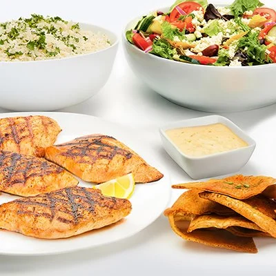 a photo of the Grilled Salmon Family Feast showing a plate with grilled salmon filets, a bowl of basmati rice, and a bowl of greek salad