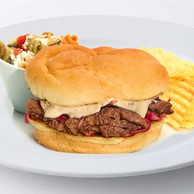 an image of the Taziki's beef sandwich with sliced beef, grilled onions, melted swiss and horseradish sauce on a kaiser roll with potato chips and pasta salad