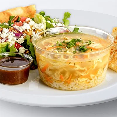 A photo of a plate with a bowl of greek lemon chicken soup and a side of mediterranean salad