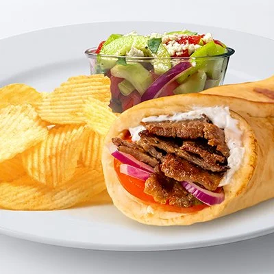 a photo of the street gyro from Taziki's with a white plate that has a gyro with sliced tomato and gyro meat accompanied with potato chips and tomato-cucumber salad