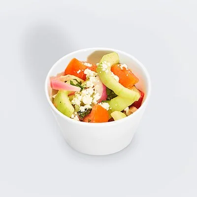 photo of a small white bowl filled with tomato cucumber salad with crumbed feta and strips of fresh basil