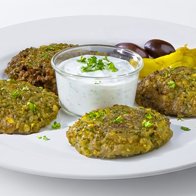 Plate with four meat patties, a bowl of white creamy sauce garnished with herbs, black and yellow olives, and yellow pepper slices.