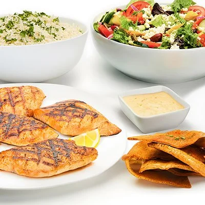 a photo of the Grilled Salmon Family Feast showing a plate with grilled salmon filets, a bowl of basmati rice, and a bowl of greek salad