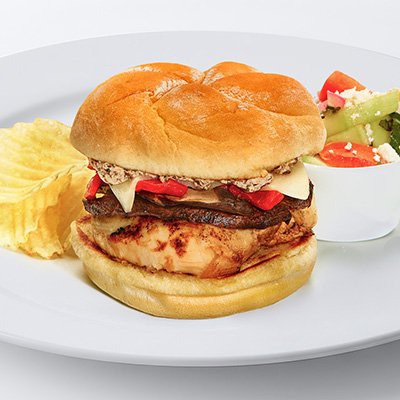 Photo of the chicken portobello sandwich, showing a kaiser bun filled with grilled chicken, roasted red peppers, swiss cheese, sliced portobello mushroom and mushroom butter, on a white plate with chips and a side of cucumber salad