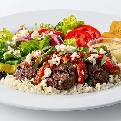 a photo of the Turkish Meatball Feast with grilled meatballs on a bed of rice topped with rustic tomato sauce, crumbled feta, and fresh basil with a side of a small greek salad